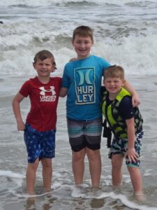 Three young boys standing ankle-deep in the water on a beach.