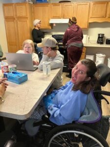 People gathered at a kitchen table and standing at a sink behind.