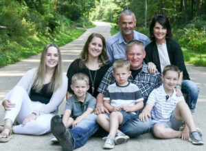 Eight people sitting outside on a nature trail for family photo.