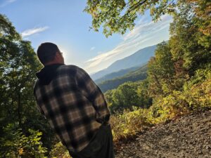 Man standing outside looking out over a landscape below.