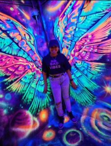 Christina posing in front of a wall with a large, psychedelic-looking, neon-colored butterfly.