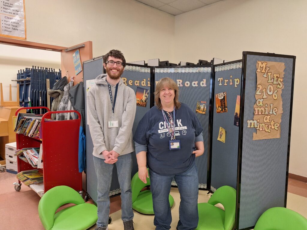 Andrew with Susan Viator standing in front of the Club K area in the school cafeteria.