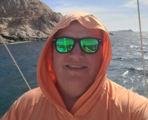 Greg Degel on a boat with water and coast in the background.