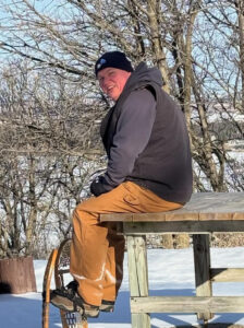 Greg Degel outside in the wintertime sitting on a wooden table.