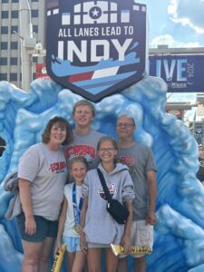 Monica Baty with her family standing in front of a sign that says "All Roads Lead to Indy."
