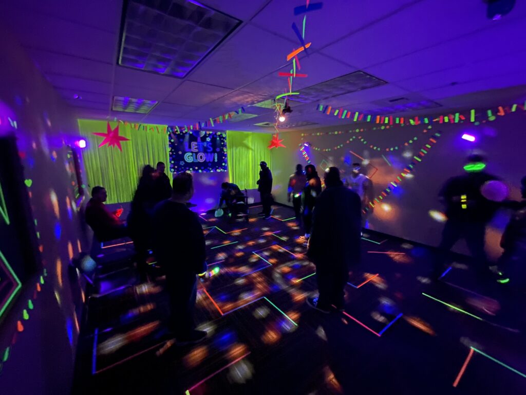 Silhouettes of people interacting in a dark room with colorful neon lights glowing.