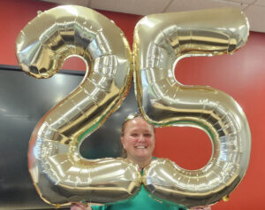 Bea Morehouse smiling and holding a giant number-25-shaped, gold balloon.