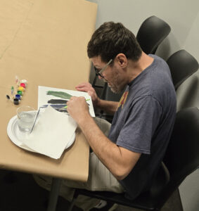 Man sitting at a table working on a painting.