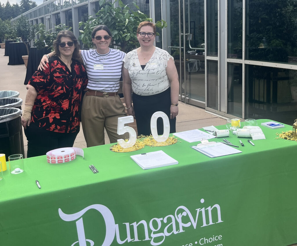 Three women standing behind a check-in table at an event.