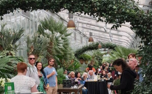 People sitting and standing in an atrium filled with green plants.