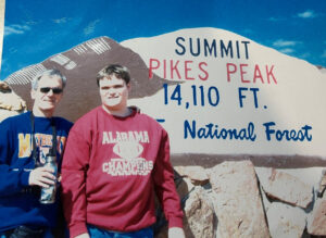 Jeff Rawlins and Chris at Pikes Peak standing in front of the National Forest sign that says they are at 14,110 feet.