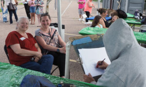Robin Fischer and her daughter sit while a caricature artist sketches their portrait.