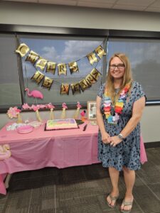 Marissa Sellner standing by a table with a pink tablecloth, decorations and a cake.