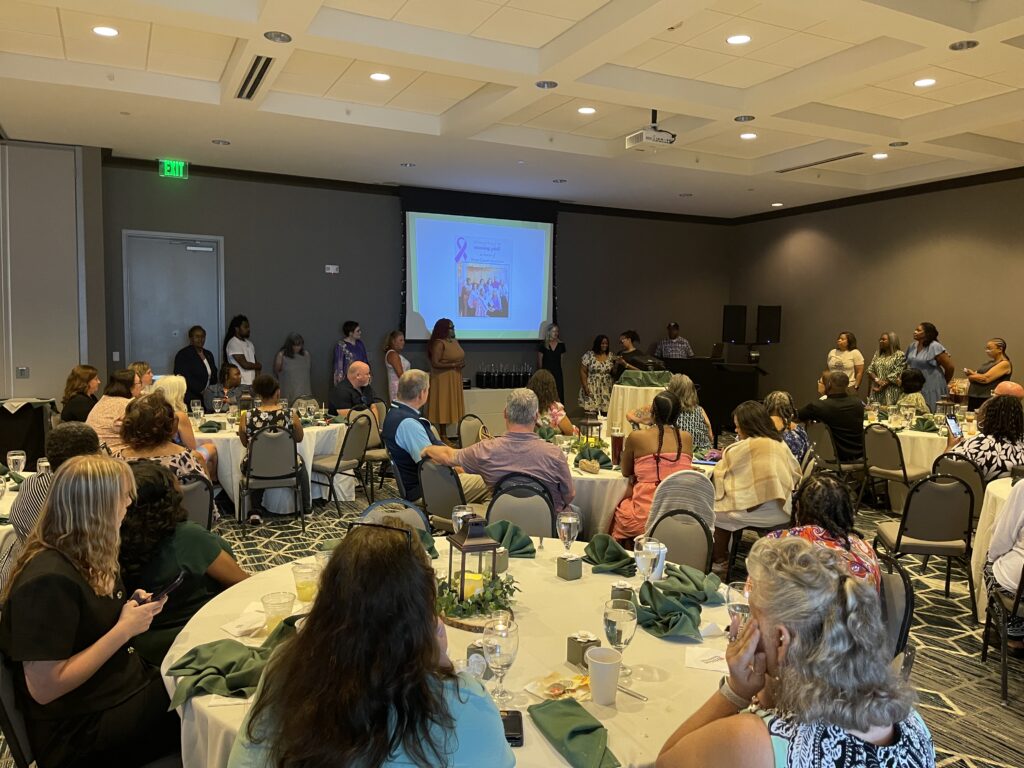 People sitting around tables in a conference room watching a presentation.