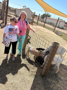 Carrie and another woman visiting a farm and looking at goats inside a pen.