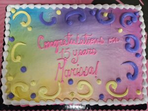 A rainbow colored rectangular cake with the words "Congratulations on 15 Years Marissa!"