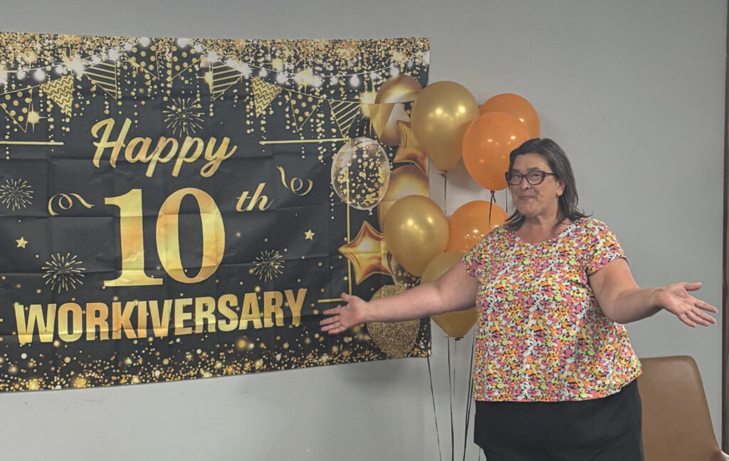 Barb Stanford standing in front of a Happy 10th Anniversary banner.