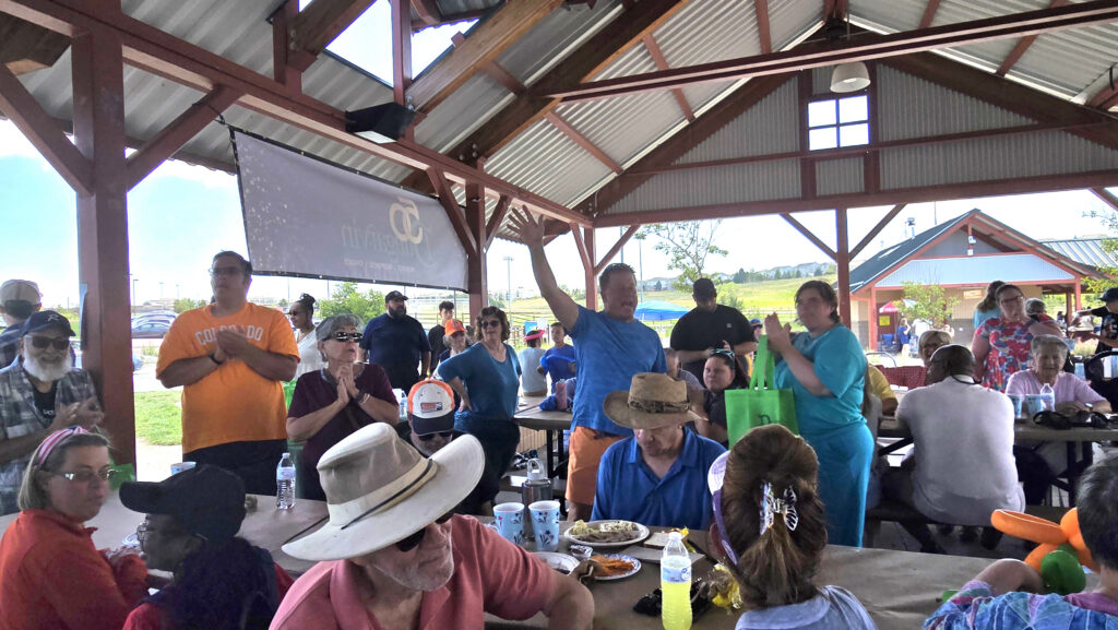 Group of people at picnic tables under a park shelter