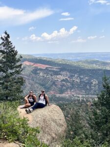 Two hikers sitting on a rock with a vista behind them.