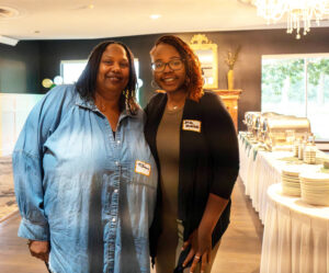 Two women smiling and standing together near a fancy buffet table in a dining hall.
