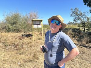 Man standing outside in nature with a camera and smiling.