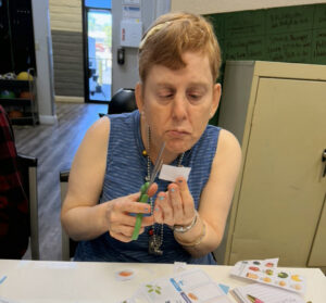 Woman sitting at a table using a scissors to cut out a small picture.