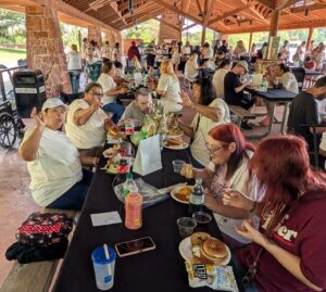 Large group of people eating lunch under a park shelter.