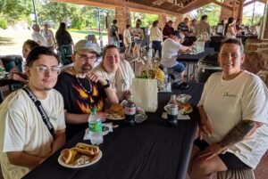 Four people sitting at a picnic table smiling at camera.