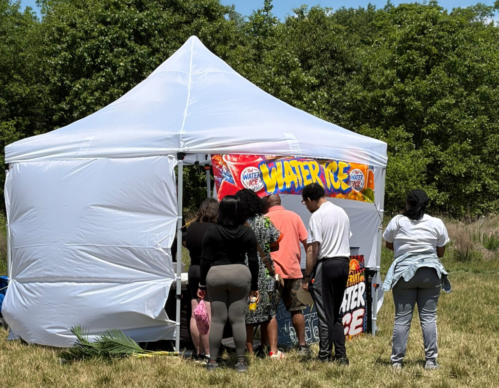 Several people standing outside of a tent waiting to get refreshments.