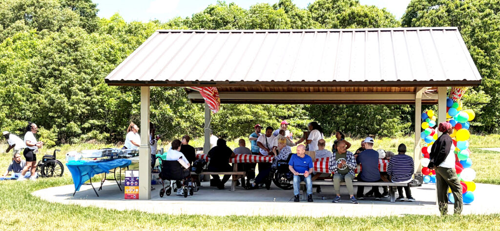 Large group sitting at picnic tables under a park shelter.